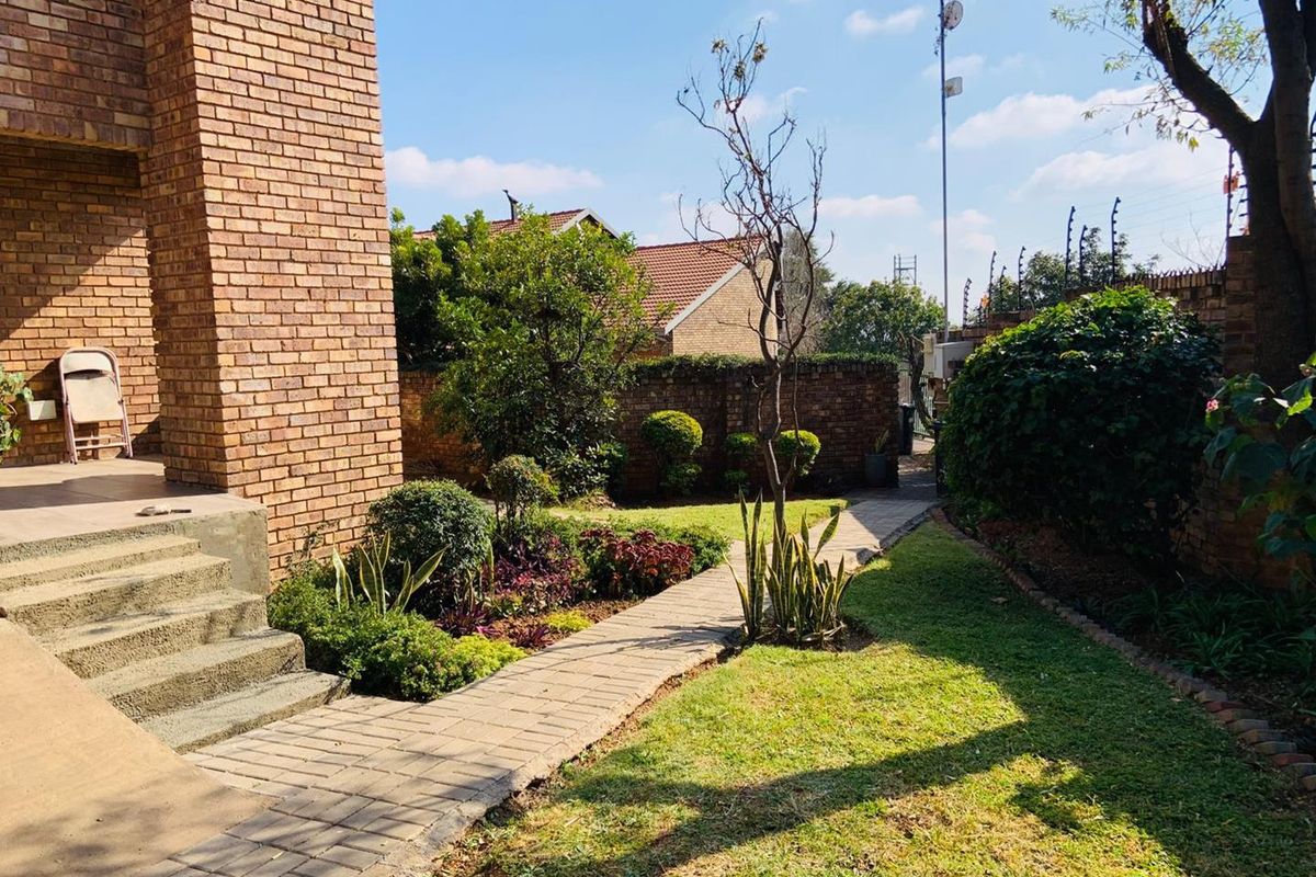 A well-maintained rear garden featuring a paved walkway, established landscaping, and brick boundary walls, providing a private outdoor space.