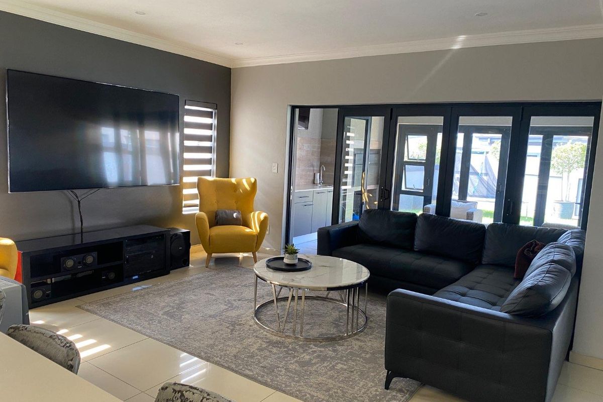 A modern living room featuring tiled flooring, recessed lighting, and large black-framed sliding doors that open to an outdoor area.
