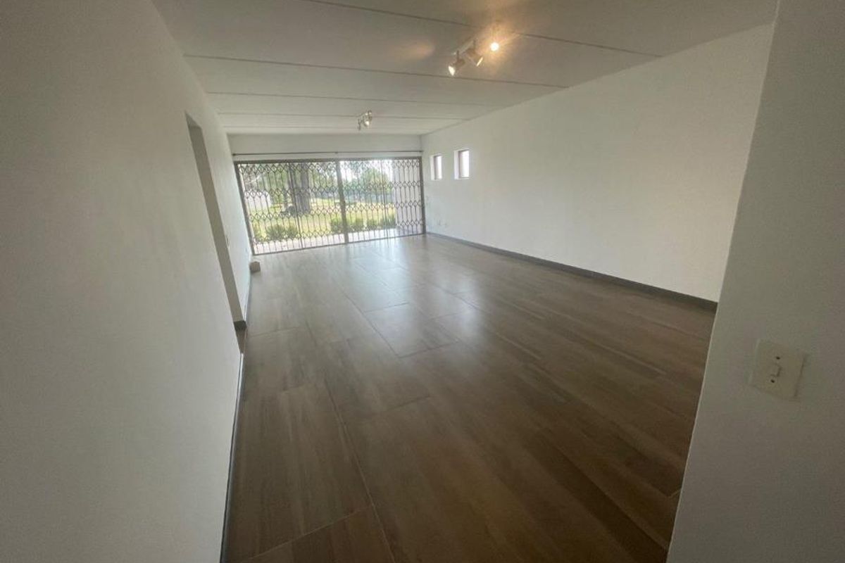 Spacious, empty living area featuring modern wood-look floor tiles, track lighting, and a large sliding door with a security gate leading outdoors.