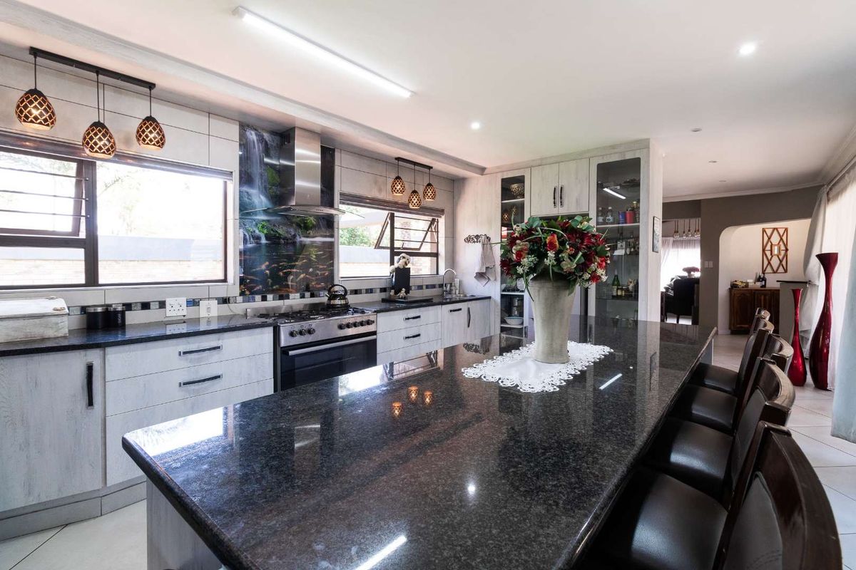 Modern kitchen featuring a large granite-topped island, built-in cabinetry, stainless steel gas stove, extractor fan, and decorative glass splashback.