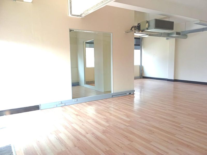 Spacious open-plan office area featuring light wood-look laminate flooring, exposed industrial-style HVAC ducting, and integrated wall-mounted electrical trunking.