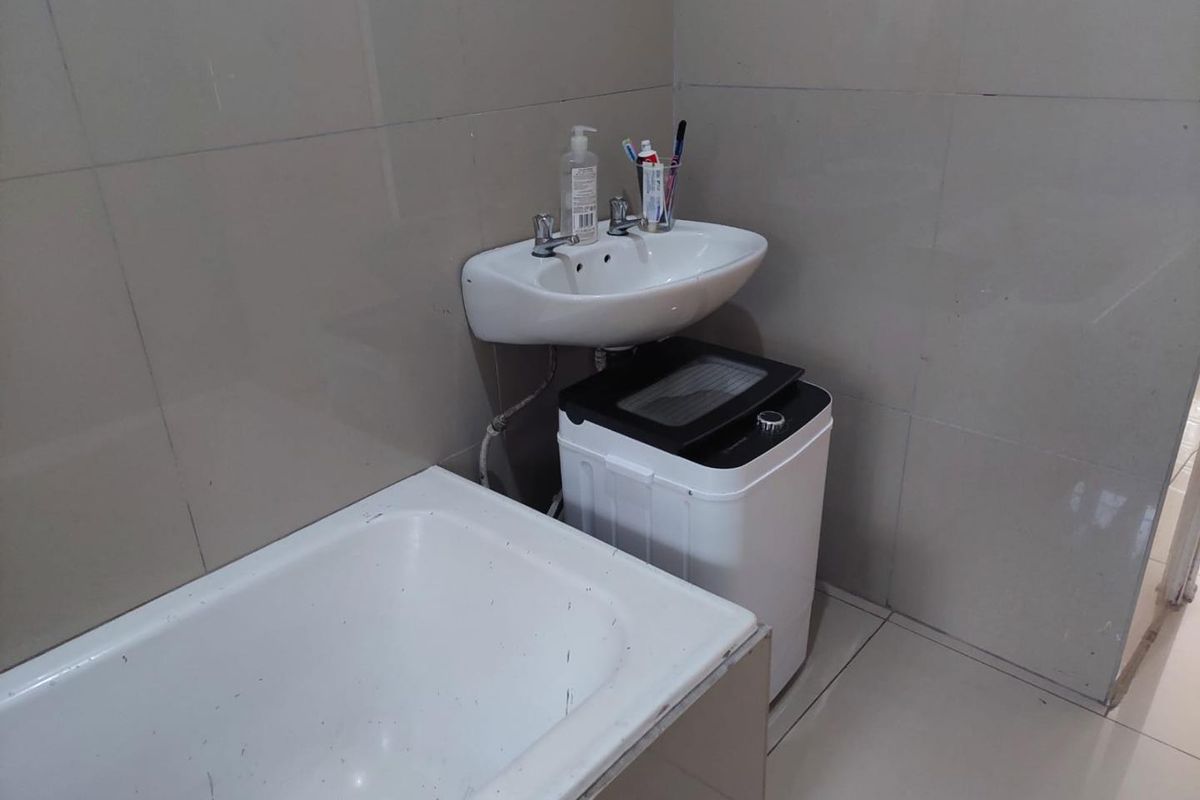 A functional bathroom featuring tiled walls and flooring, a wall-mounted basin, and a bathtub.
