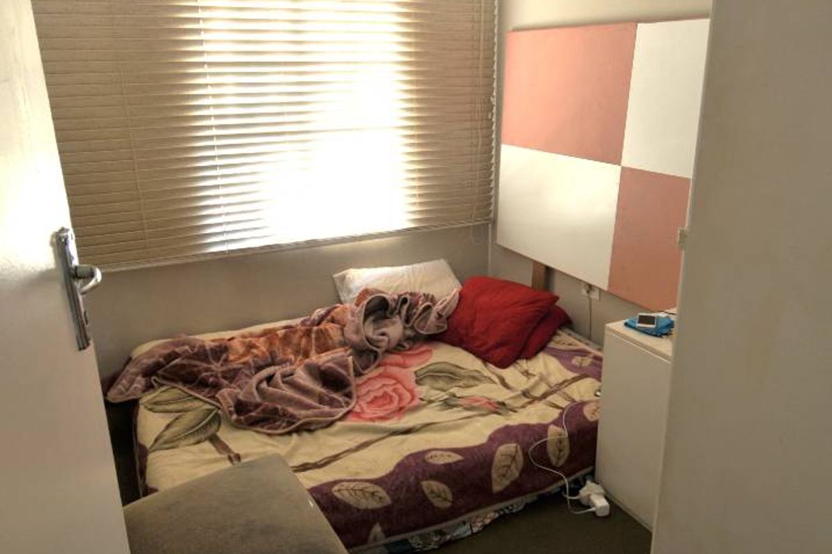 A compact bedroom featuring a window with fitted blinds and a wall-mounted headboard panel.