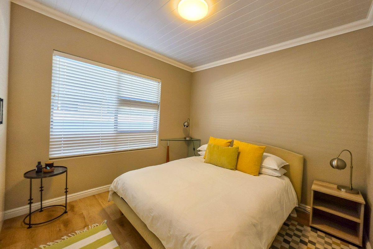 A well-maintained bedroom featuring timber-look flooring, a tongue and groove ceiling, and venetian blinds, offering a comfortable and neutral living space.