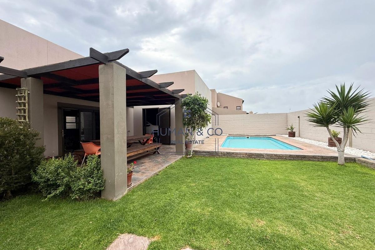 Rear garden featuring a swimming pool, paved patio area with a pergola, and a well-maintained lawn.