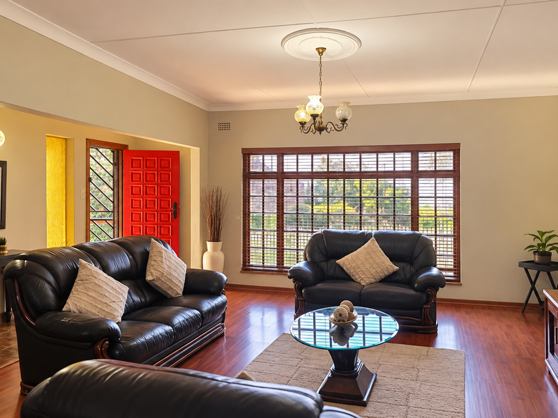A well-maintained living room featuring warm laminate flooring, large wooden-framed windows, and classic ceiling detailing, creating a comfortable and inviting atmosphere.