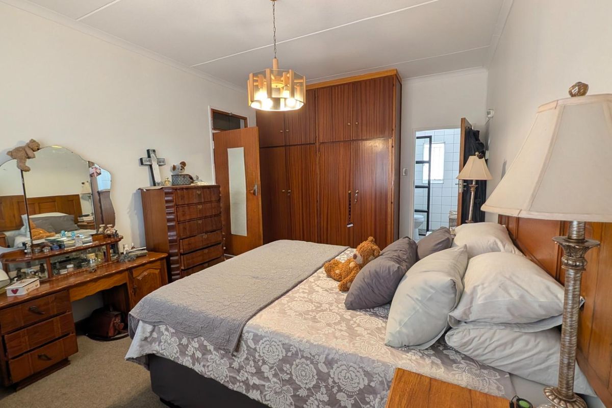 A bedroom featuring built-in wooden wardrobes, carpeted flooring, and a central ceiling light fixture, with an adjoining bathroom visible through the doorway.