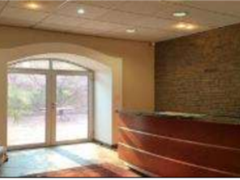 Office reception area featuring an exposed brick feature wall, built-in reception desk, and arched glass double doors leading to the exterior.