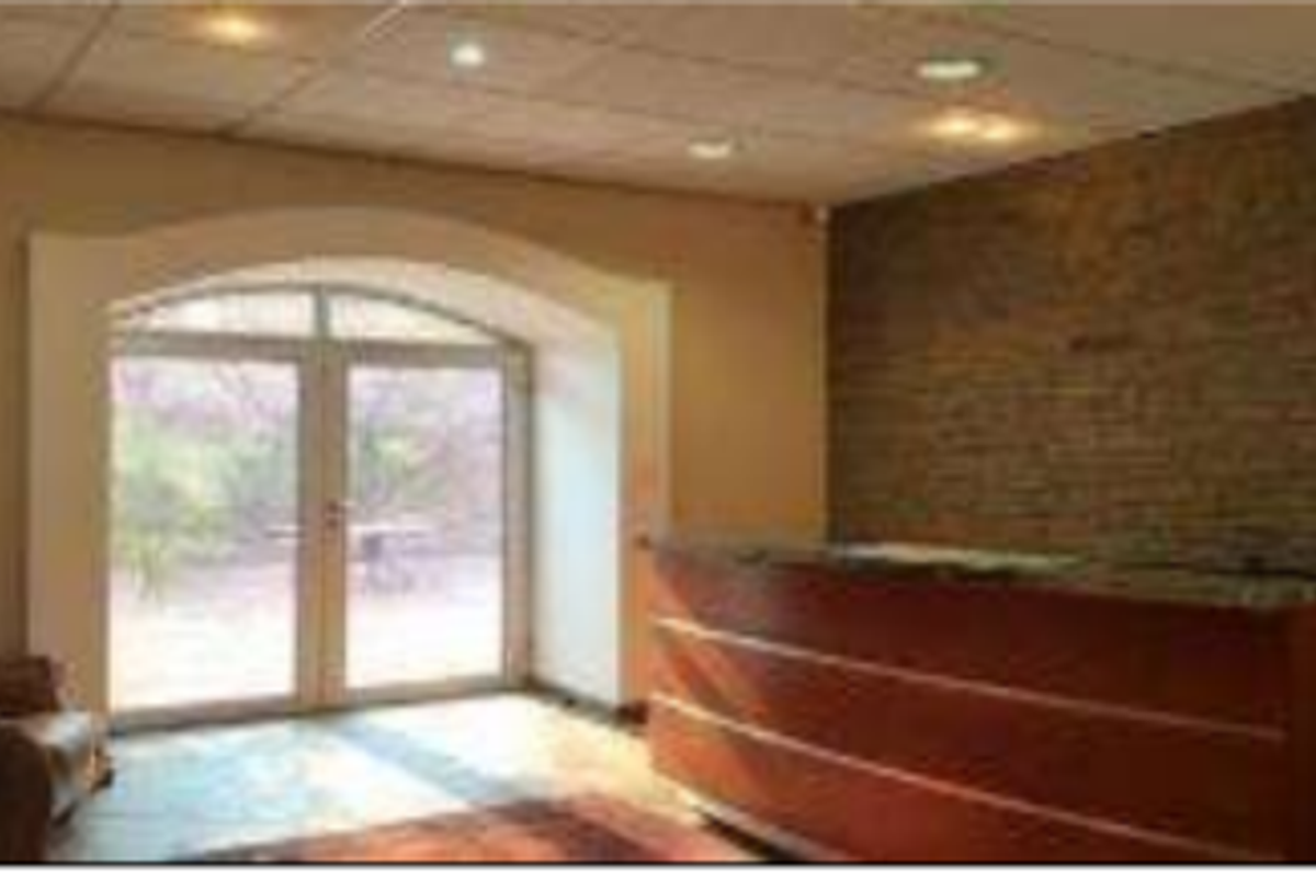 Office reception area featuring an exposed brick feature wall, built-in reception desk, and arched glass double doors leading to the exterior.
