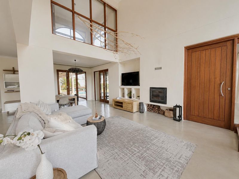 Spacious open-plan living area featuring double-volume ceilings, polished concrete floors, a built-in fireplace, and large timber doors leading to the outdoor space.