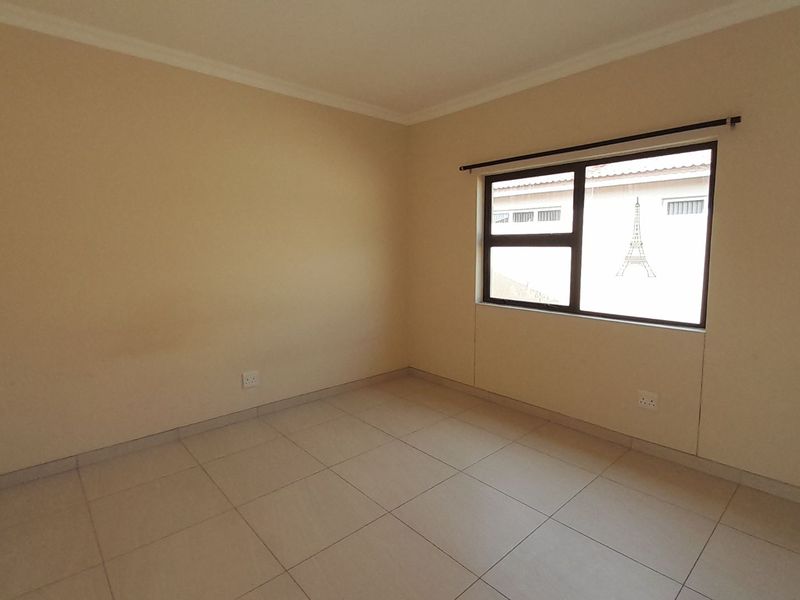 A clean, empty bedroom featuring neutral tiled flooring, coving, and an aluminium-framed window, providing a blank canvas for personalization.