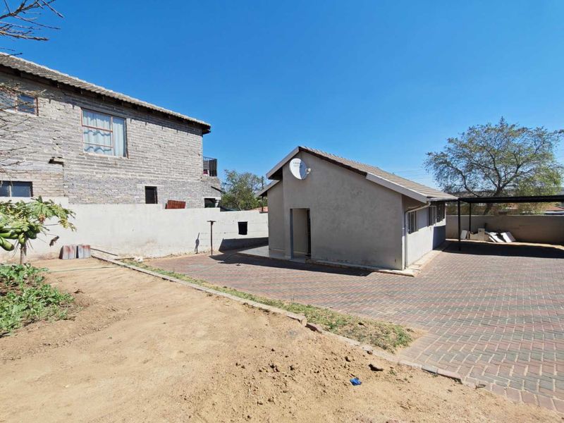 Rear exterior view of the property featuring a paved driveway, boundary wall, and a detached structure with a tiled roof.