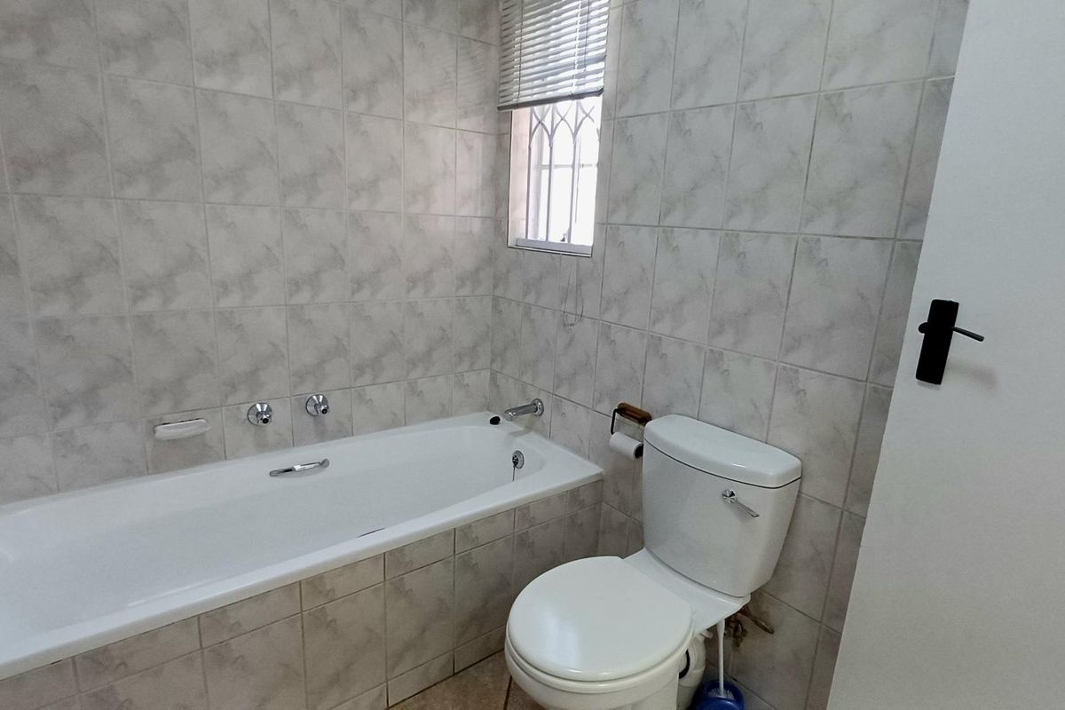 A functional bathroom featuring a built-in bathtub, toilet, and neutral wall tiling with a window providing natural light.