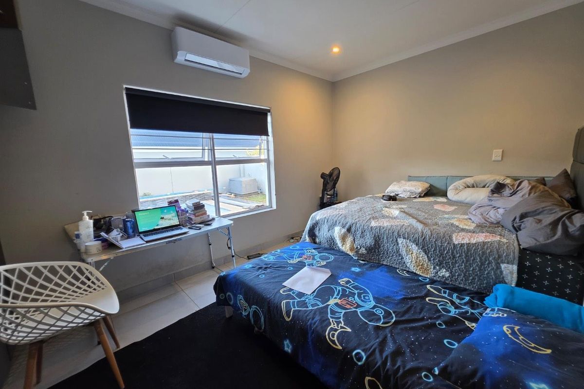 A bedroom featuring tiled flooring, a wall-mounted air conditioning unit, and a large window providing natural light.