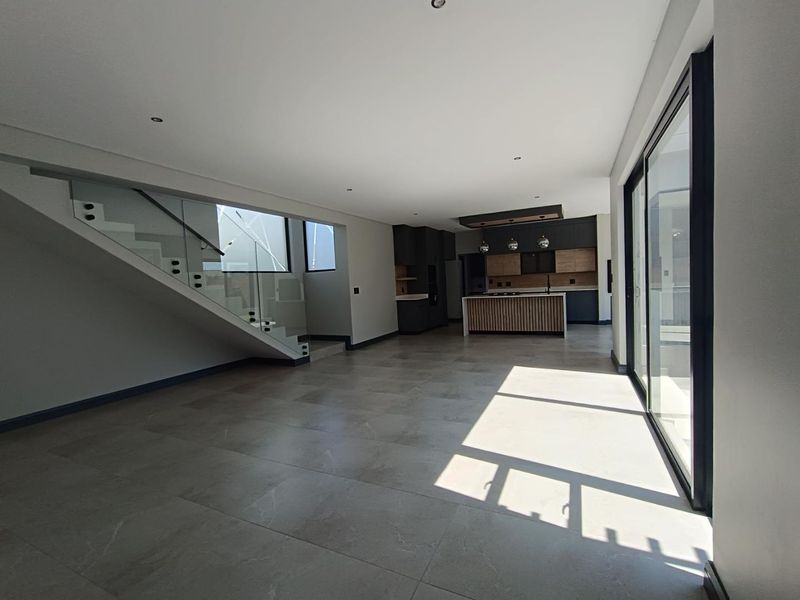 Spacious open-plan living area featuring a modern kitchen with island, sleek staircase with glass balustrade, and large sliding doors leading to the exterior.