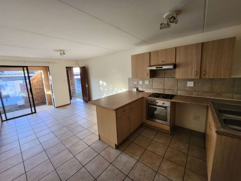 Open plan kitchen and living area featuring laminate cabinetry, built-in oven, hob, and tiled flooring with direct access to an outdoor patio area.