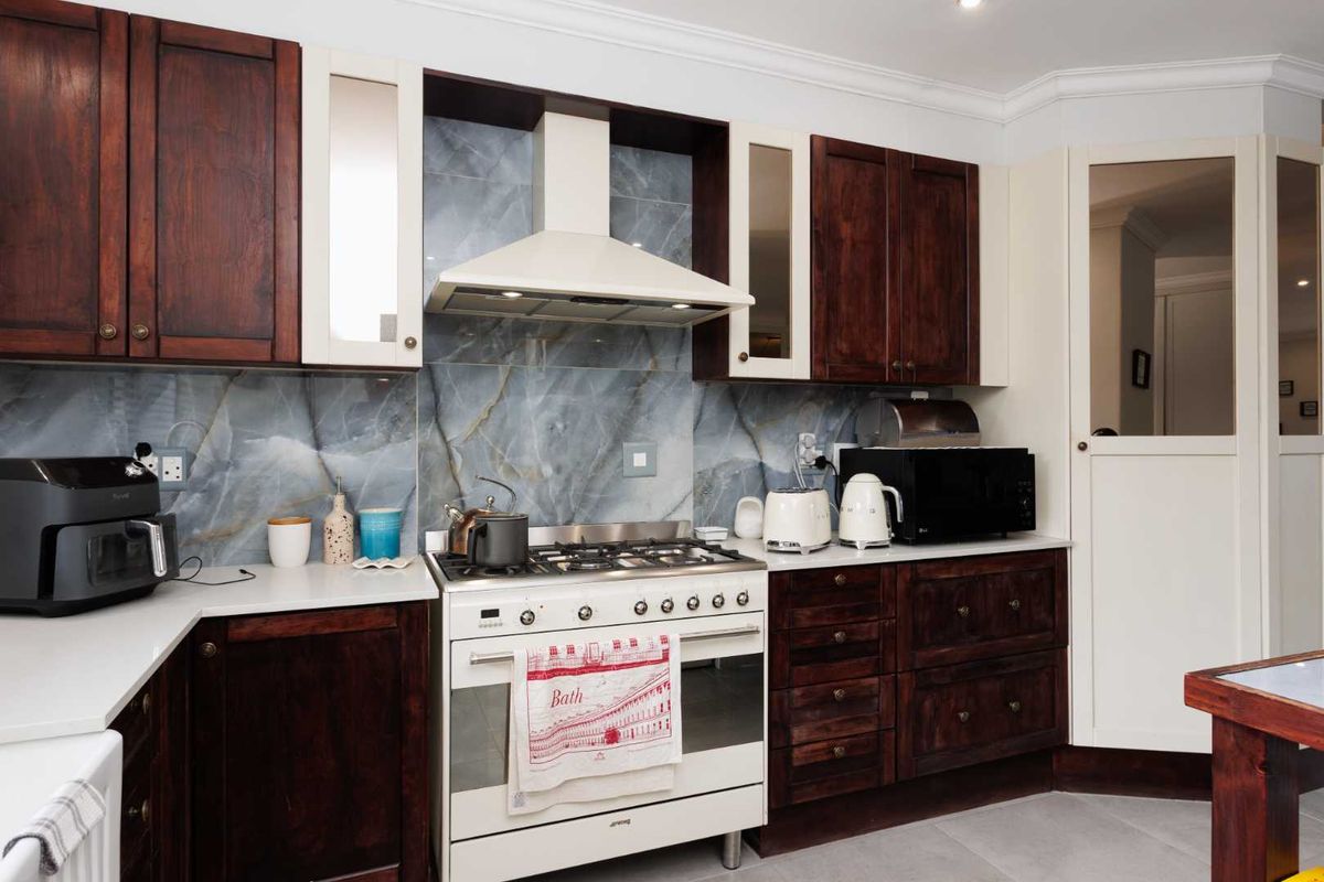 A well-appointed kitchen featuring dark wood cabinetry, contrasting cream accents, a stone-look splashback, and a professional-style gas range with an integrated extractor fan.