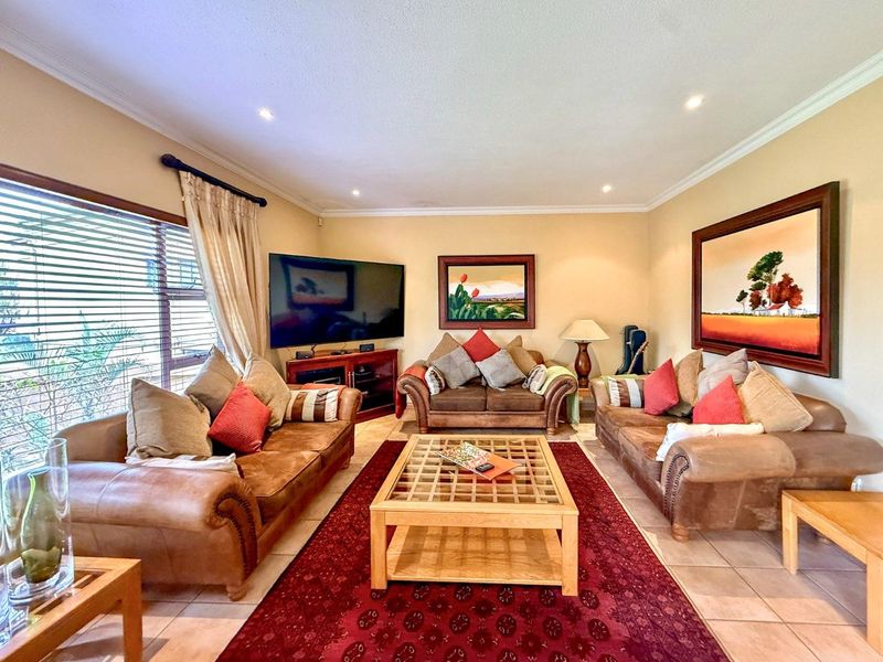 A comfortable living room featuring tiled flooring, recessed downlighting, and large windows with venetian blinds, creating a warm and inviting space.
