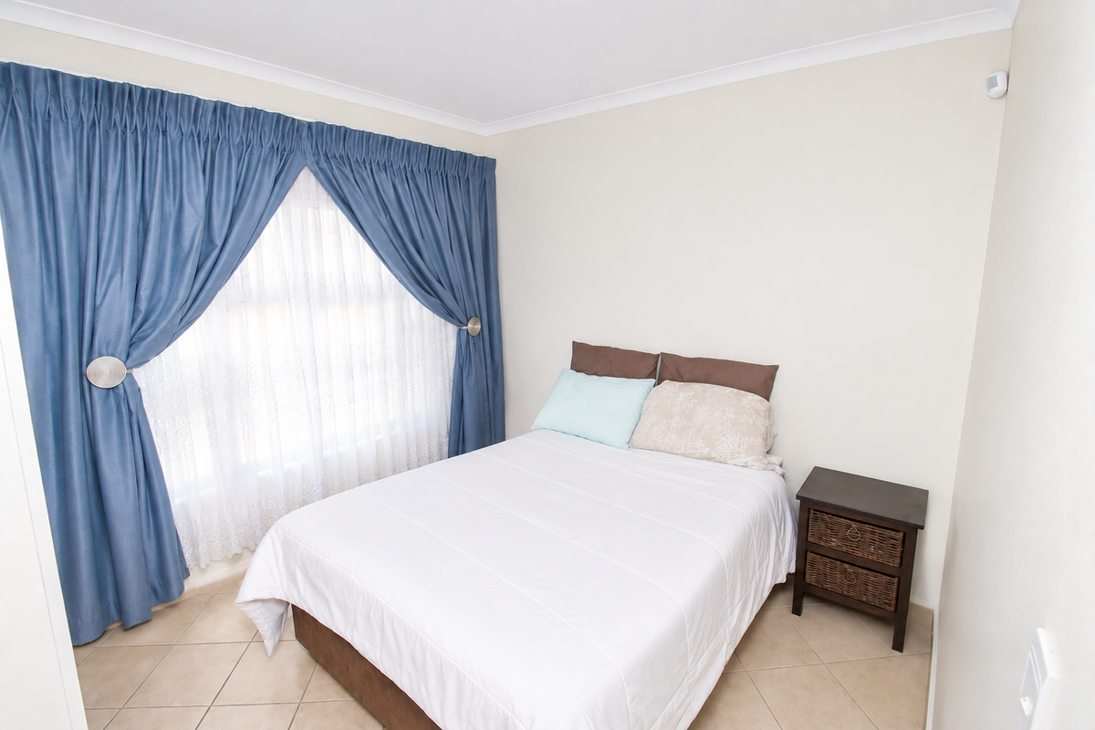 A bright bedroom featuring tiled flooring, neutral walls, and a window dressed with blue curtains.