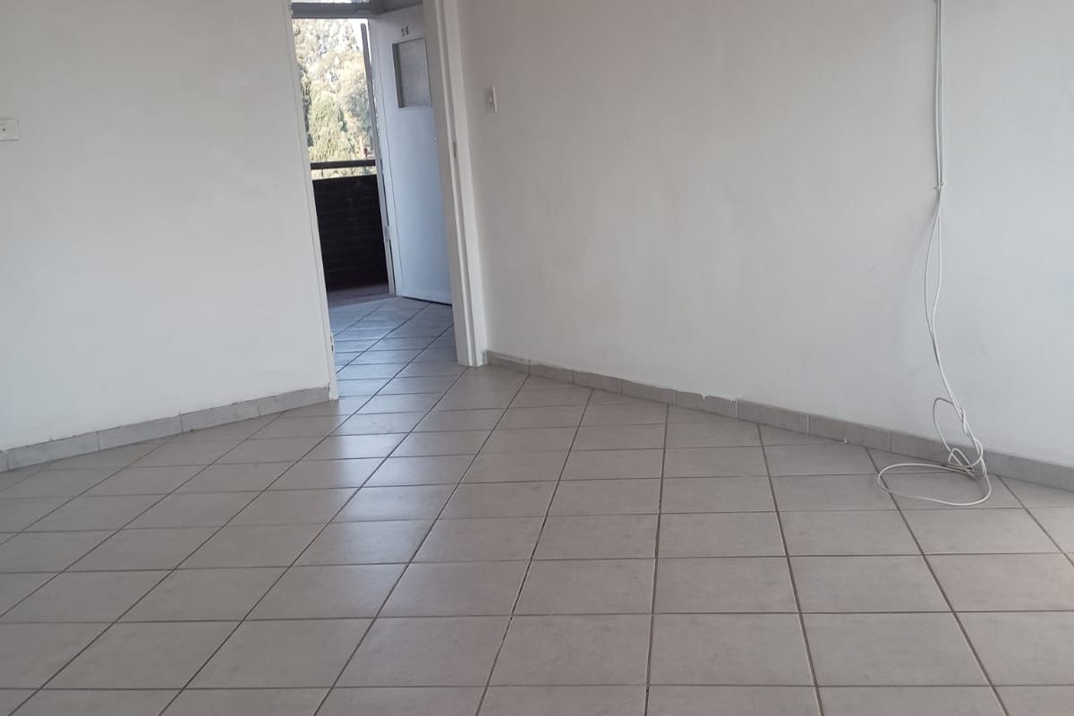 An empty living room featuring neutral ceramic floor tiles, coved ceiling cornices, and a doorway leading to an outdoor balcony area.