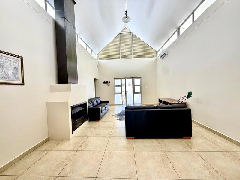 Spacious living room featuring a high vaulted ceiling, tiled flooring, a built-in fireplace, and large windows that provide ample natural light.