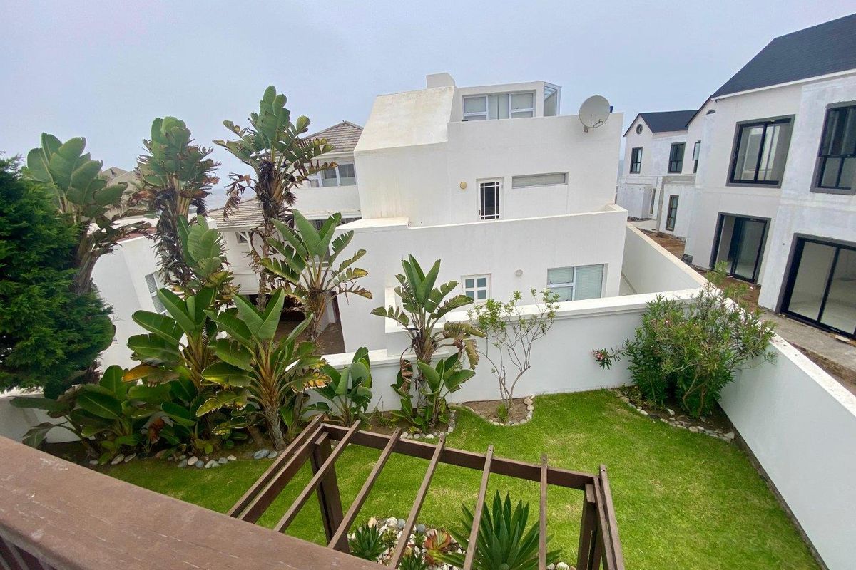 A view of the rear garden and courtyard area featuring a wooden pergola, landscaped lawn, and established plantings against the townhouse exterior.