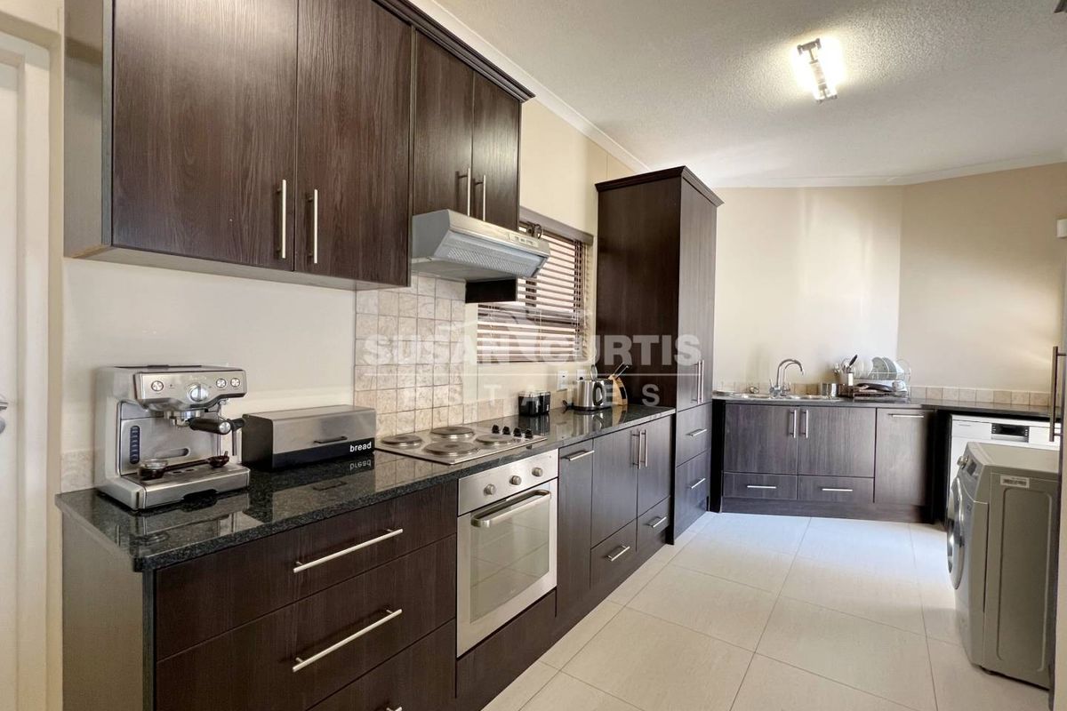 A modern kitchen featuring dark wood cabinetry, granite countertops, a built-in oven, hob, and extractor fan, with tiled flooring throughout.