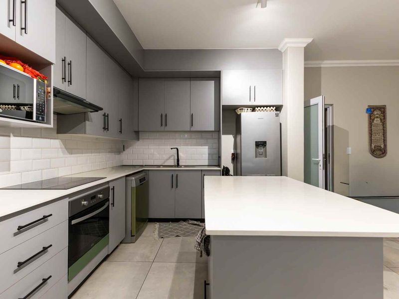 Modern kitchen featuring grey cabinetry, white quartz countertops, a central island, subway tile backsplash, and integrated appliances.