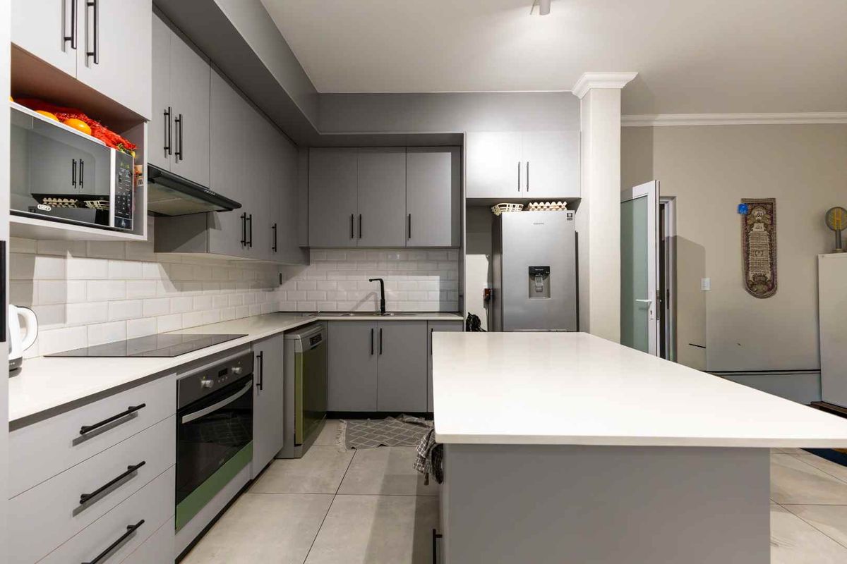 Modern kitchen featuring grey cabinetry, white quartz countertops, a central island, subway tile backsplash, and integrated appliances.