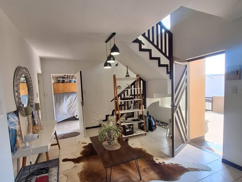 A bright living area featuring tiled flooring, a modern staircase, and direct access to an outdoor patio space.