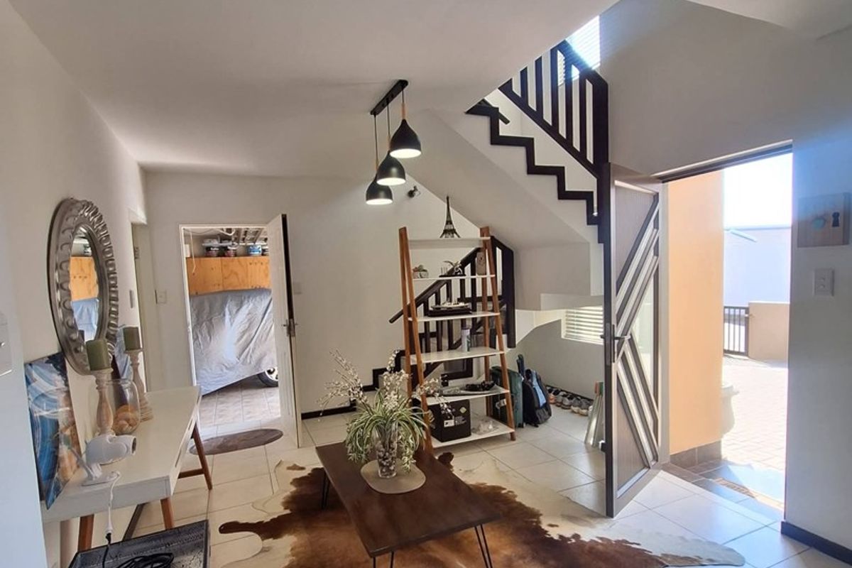 A bright living area featuring tiled flooring, a modern staircase, and direct access to an outdoor patio space.