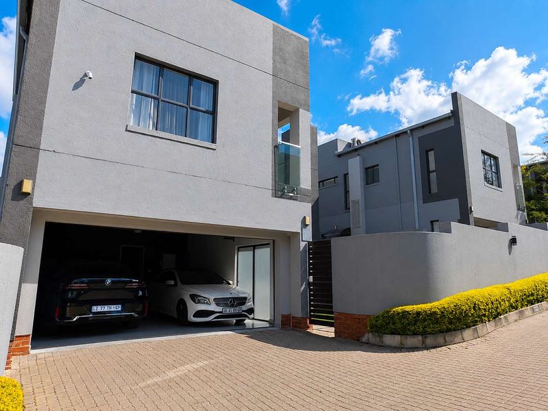 Modern double-storey cluster home featuring a paved driveway, integrated double garage, and contemporary grey facade with glass balcony detailing.