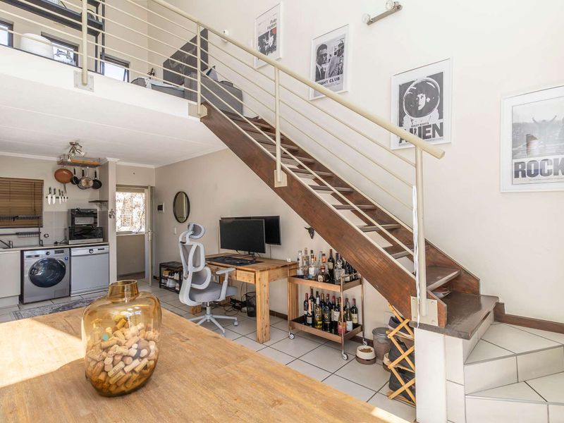 Open-plan living area featuring a mezzanine level, a wooden staircase with metal balustrades, and a compact kitchen space with tiled flooring.