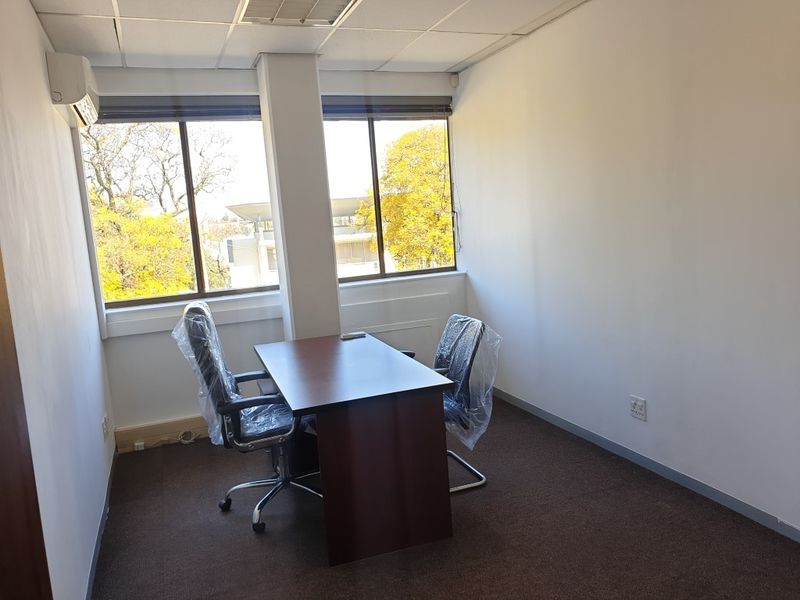 A functional office space featuring carpeted flooring, a suspended ceiling, split-system air conditioning, and large windows providing natural light.