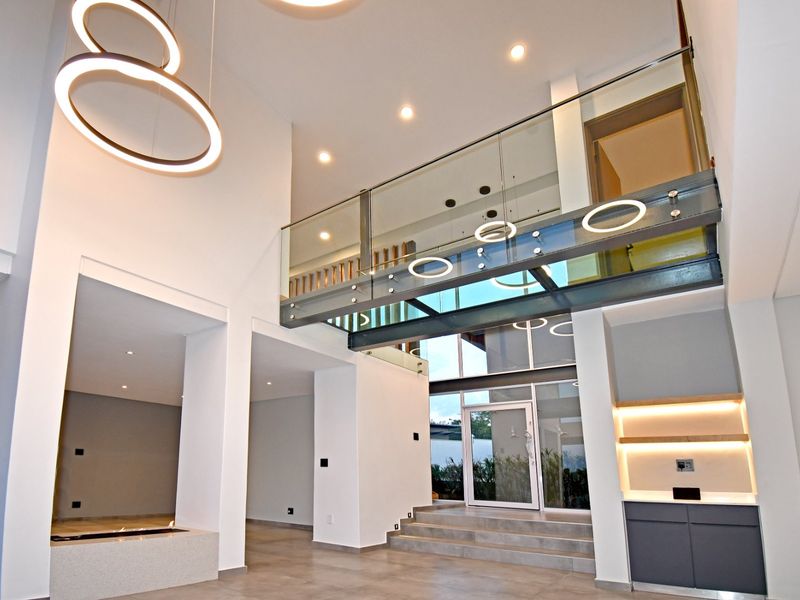 Spacious double-volume entrance hall featuring a modern glass mezzanine, contemporary lighting, built-in cabinetry, and a sleek stone fireplace.