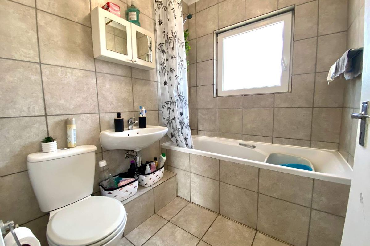 A functional bathroom featuring a bathtub with shower attachment, wall-mounted basin, toilet, and neutral floor-to-ceiling tiling.