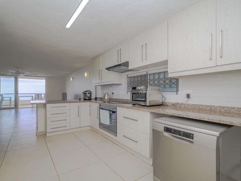 Open-plan kitchen featuring white cabinetry, granite countertops, and subway tile backsplash, flowing into a living area with balcony access and ocean views.