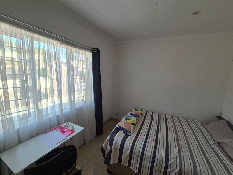 A functional bedroom featuring tiled flooring, recessed ceiling lights, and a large window fitted with security bars for added safety.
