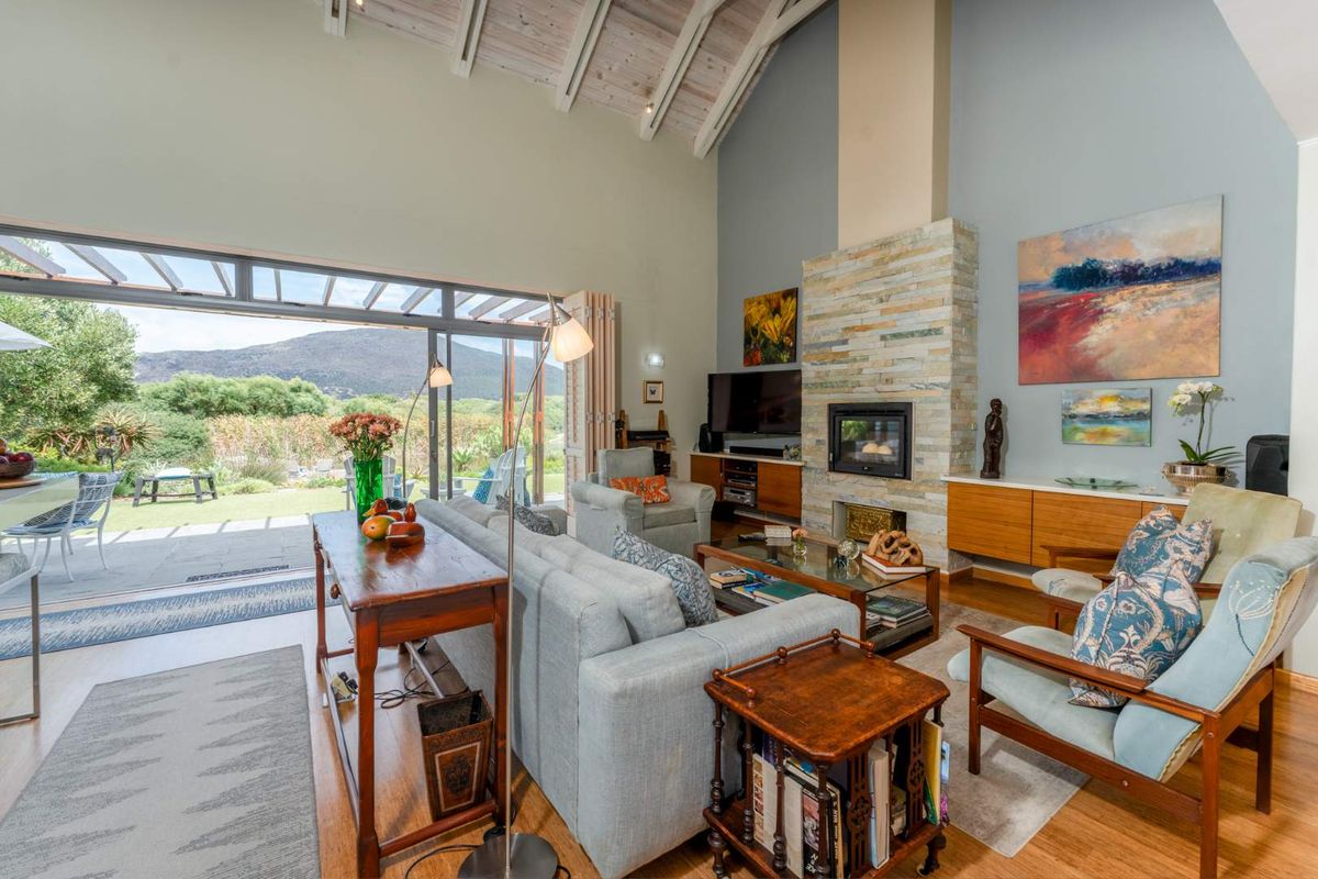 Spacious living room featuring a high vaulted ceiling, stone-clad fireplace, and large sliding doors opening to a scenic outdoor patio and garden area.