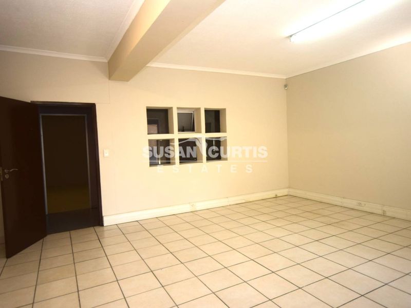A clean, empty office space featuring tiled flooring, fluorescent lighting, and an internal window, suitable for a professional workspace.
