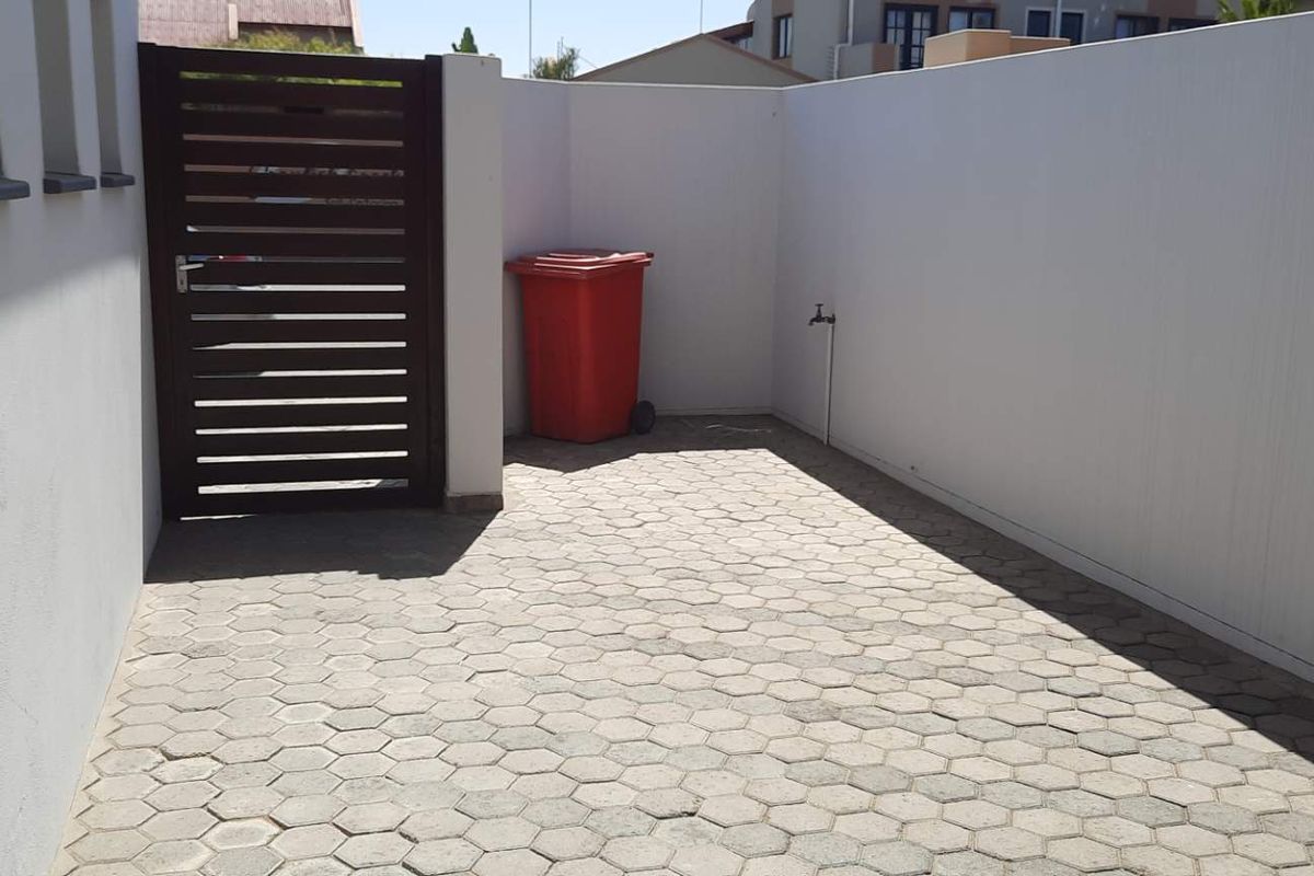A paved outdoor courtyard area featuring high boundary walls, a secure pedestrian gate, and an external water tap.