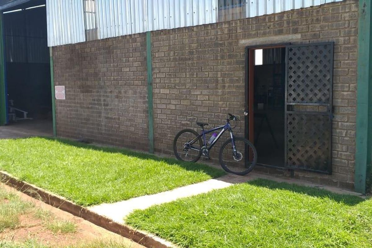 Exterior view of an industrial warehouse building featuring brick walls, corrugated metal cladding, and a secure metal security gate entrance.