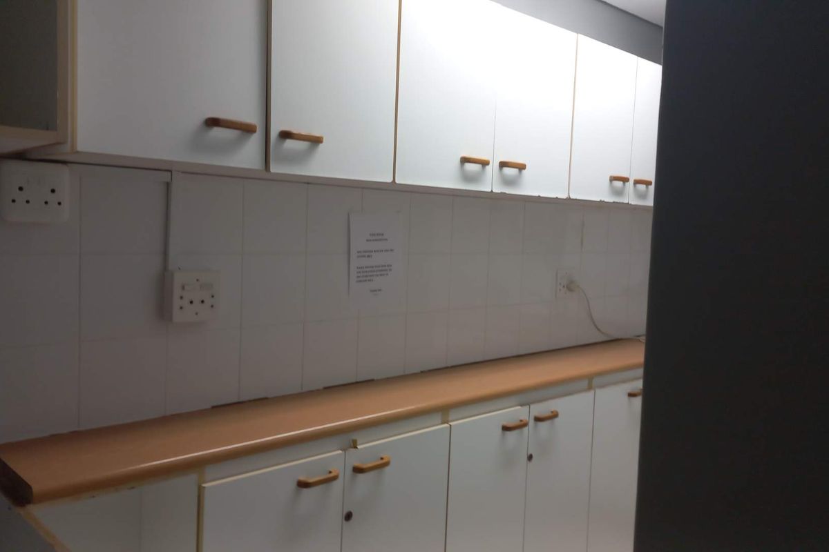 A functional office kitchenette featuring white cabinetry, laminate countertops, and tiled splashbacks with integrated electrical outlets.