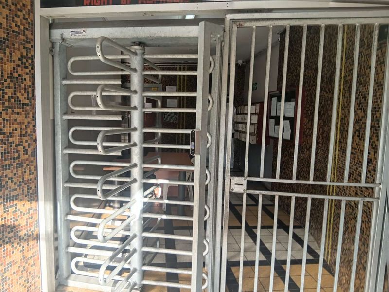 Building entrance area featuring a security turnstile, metal gate, mosaic wall tiling, and tiled flooring.