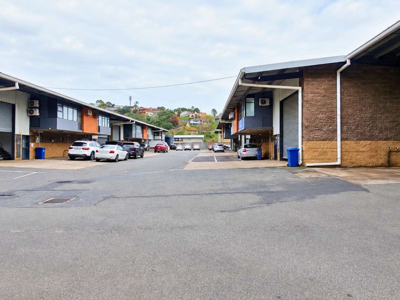 Exterior view of an industrial complex featuring multiple units with roller shutter doors, brick facades, and a shared asphalt driveway.
