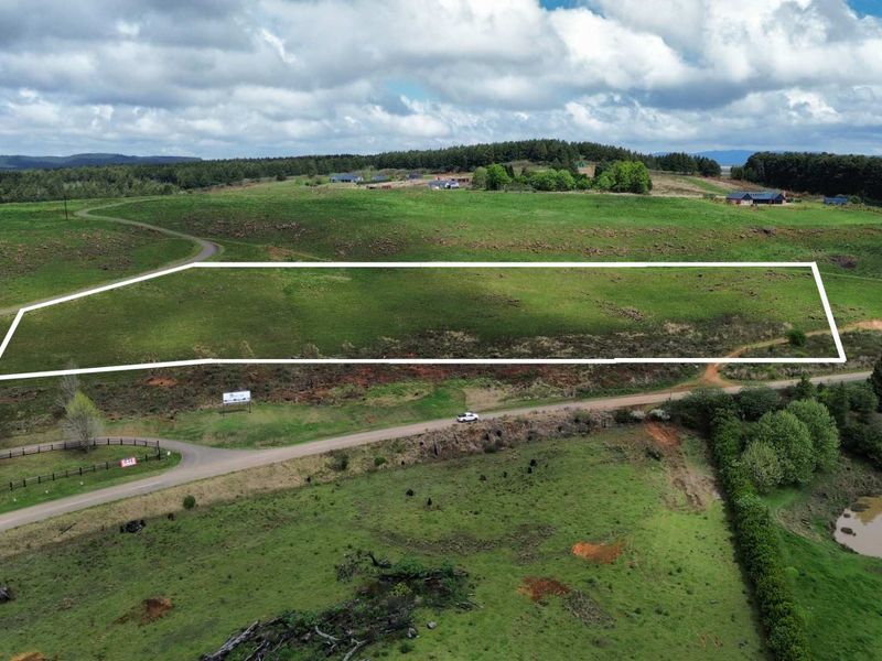 An aerial view of a large, undeveloped residential plot of land featuring open grassland and surrounding rural landscape.