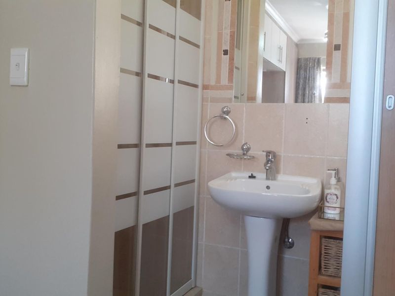 A functional bathroom featuring a pedestal basin, tiled splashback, wall mirror, and a sliding shower door enclosure.