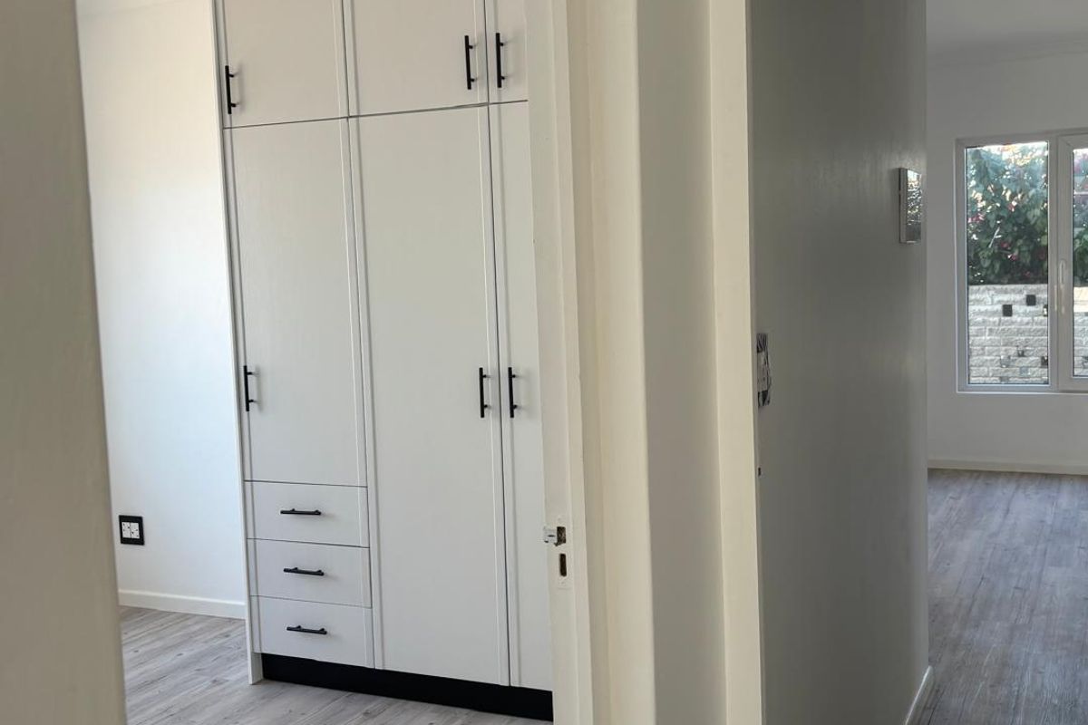 A bright bedroom featuring modern built-in cabinetry with integrated drawers and light-toned wood-look flooring.