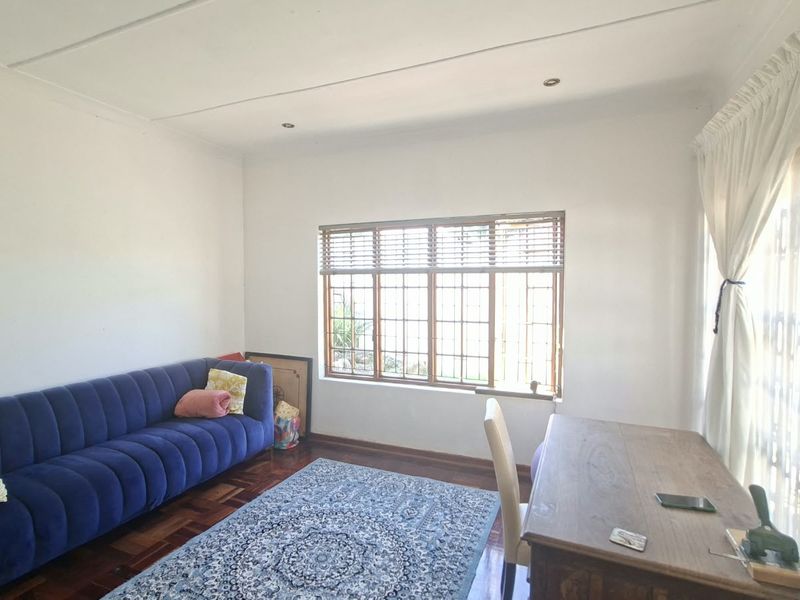 A bright living room featuring classic parquet flooring, large windows with wooden frames, and recessed ceiling lighting, offering a comfortable and versatile living space.