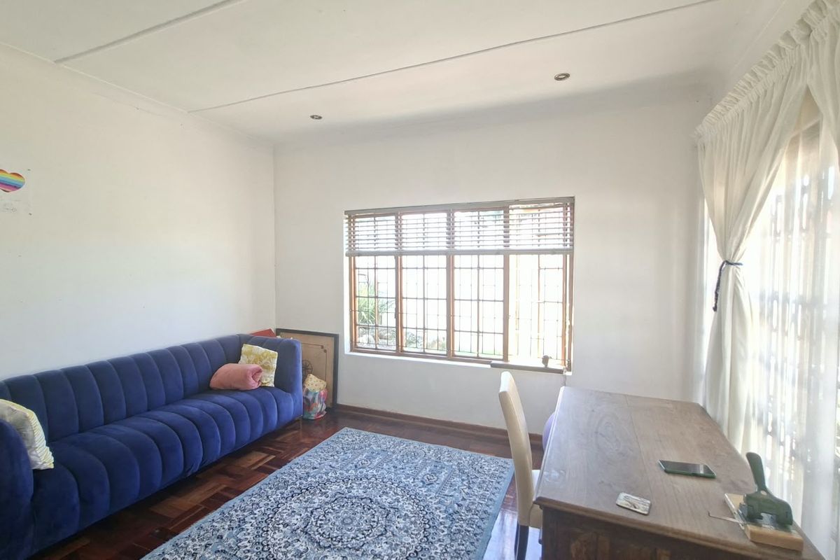 A bright living room featuring classic parquet flooring, large windows with wooden frames, and recessed ceiling lighting, offering a comfortable and versatile living space.